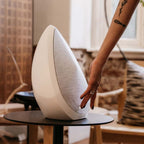 White wireless speaker on a round base, being placed by hand
