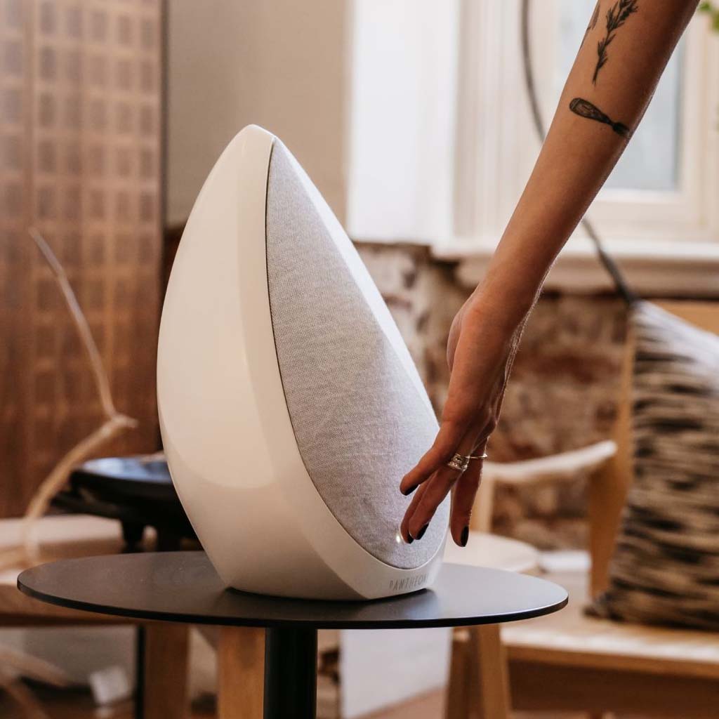 White wireless speaker on a round base, being placed by hand